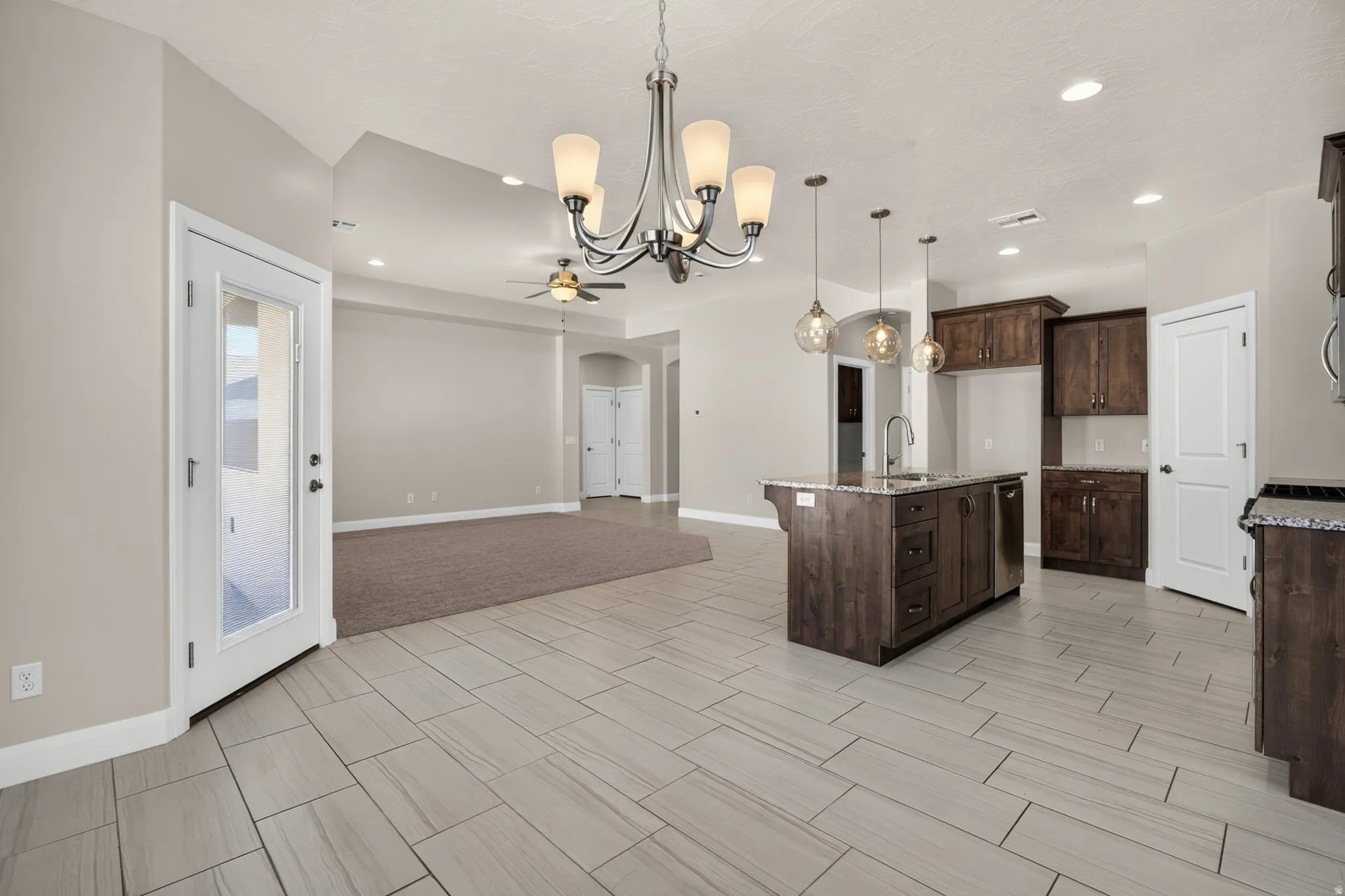 Open-concept living space with vaulted ceilings, large format tile flooring, a kitchen island with pendant lighting, and dark wood-finish cabinetry