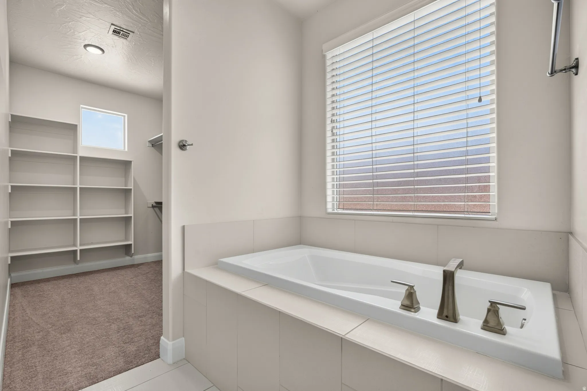 Recessed soaking tub with brushed nickel fixtures, tile surround, and privacy blinds
