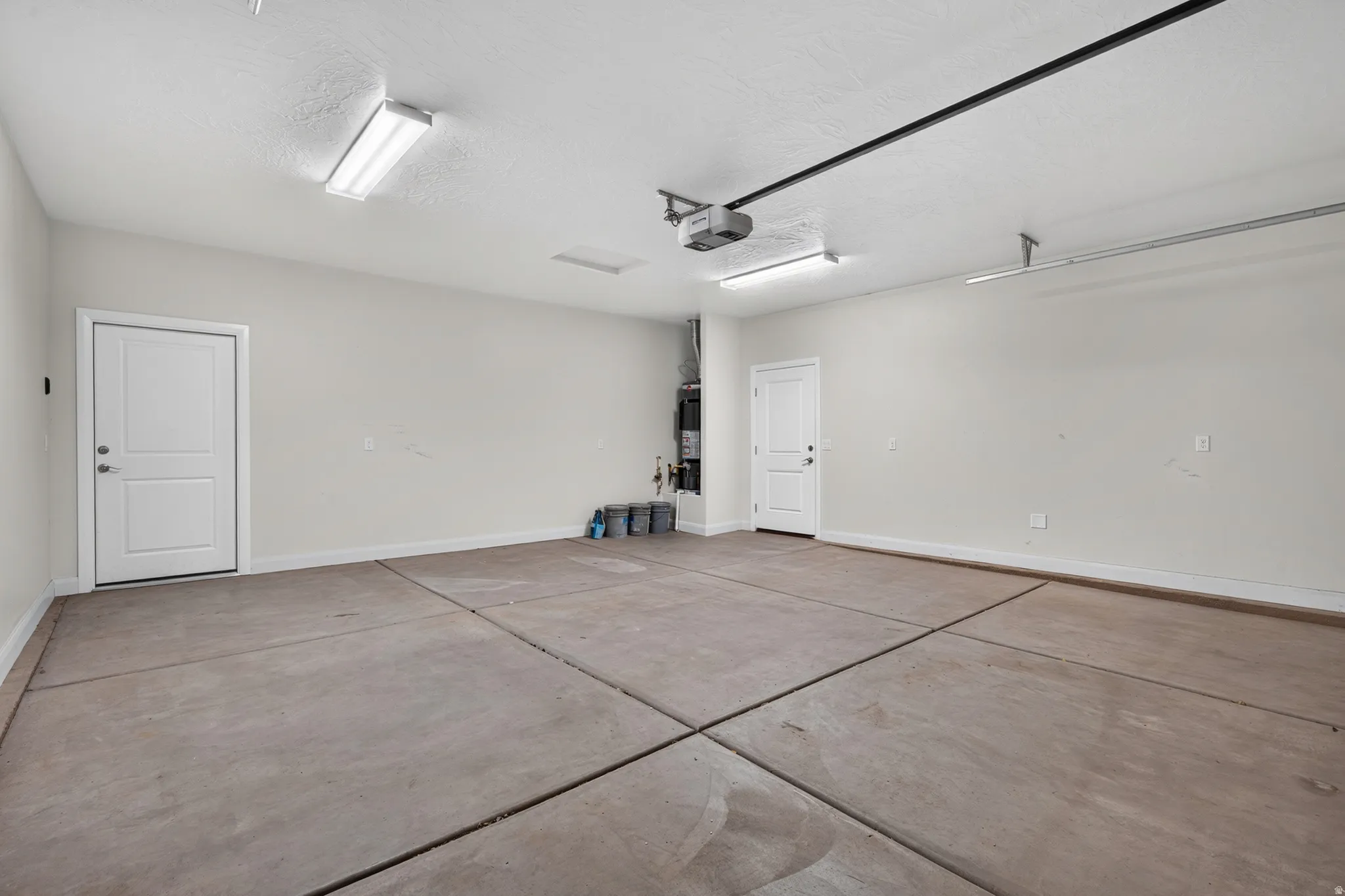 Spacious garage with light gray walls, two bright overhead light fixtures, a garage door opener mechanism, and a concrete floor