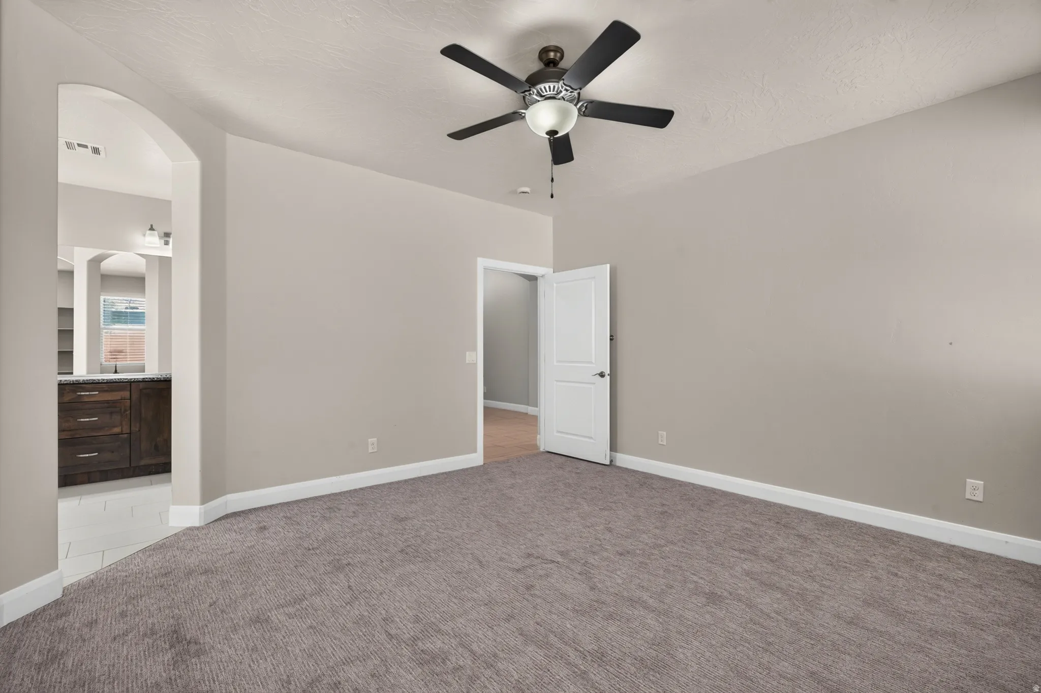 Arched entryway leading to an interior space with dark wood-finish cabinetry, a built-in ceiling fan, and light gray wall tones