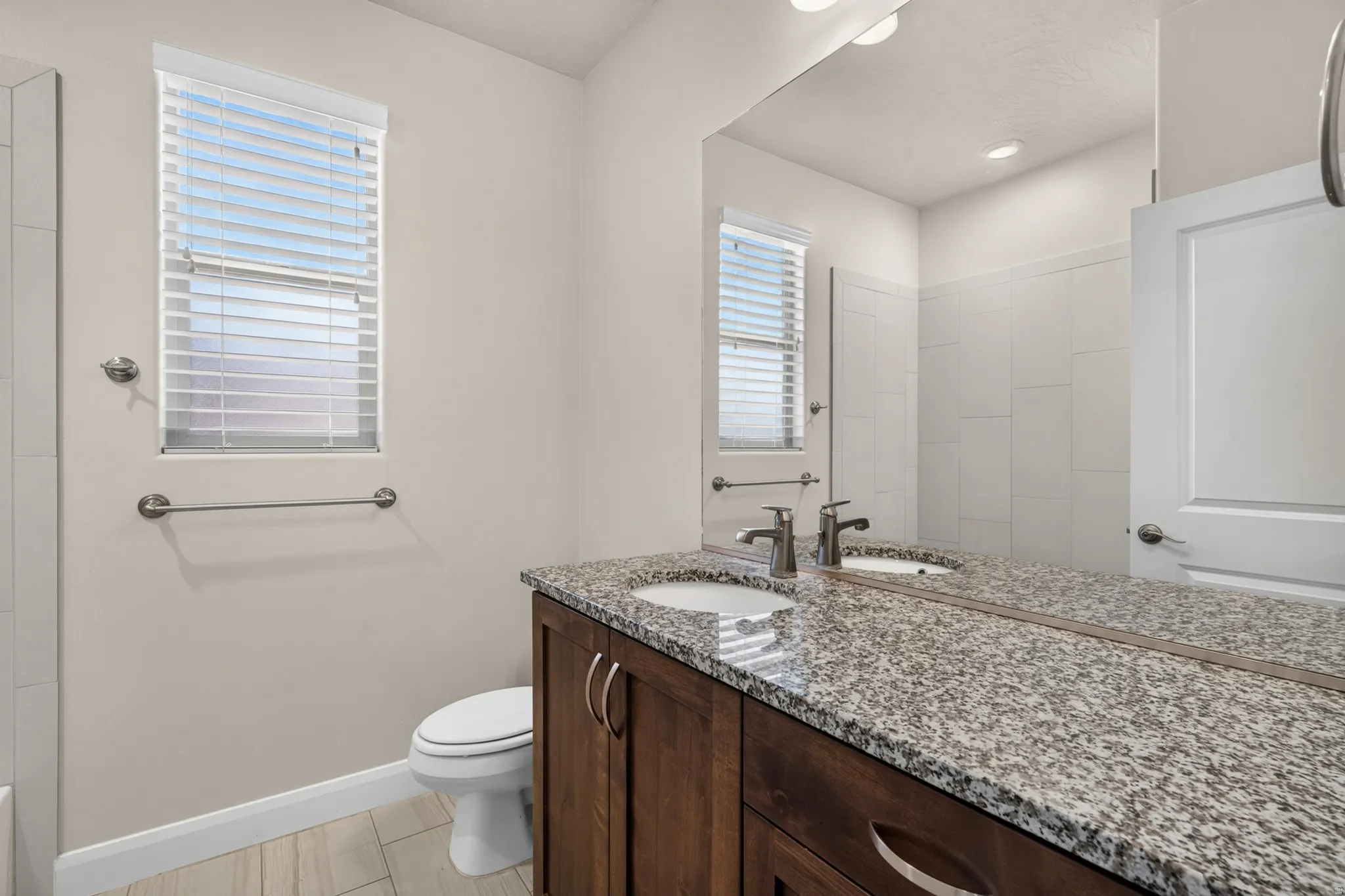 Dual vanity with undermount sinks and extensive countertop space, wood-finish cabinetry, neutral wall color, and a window with blinds