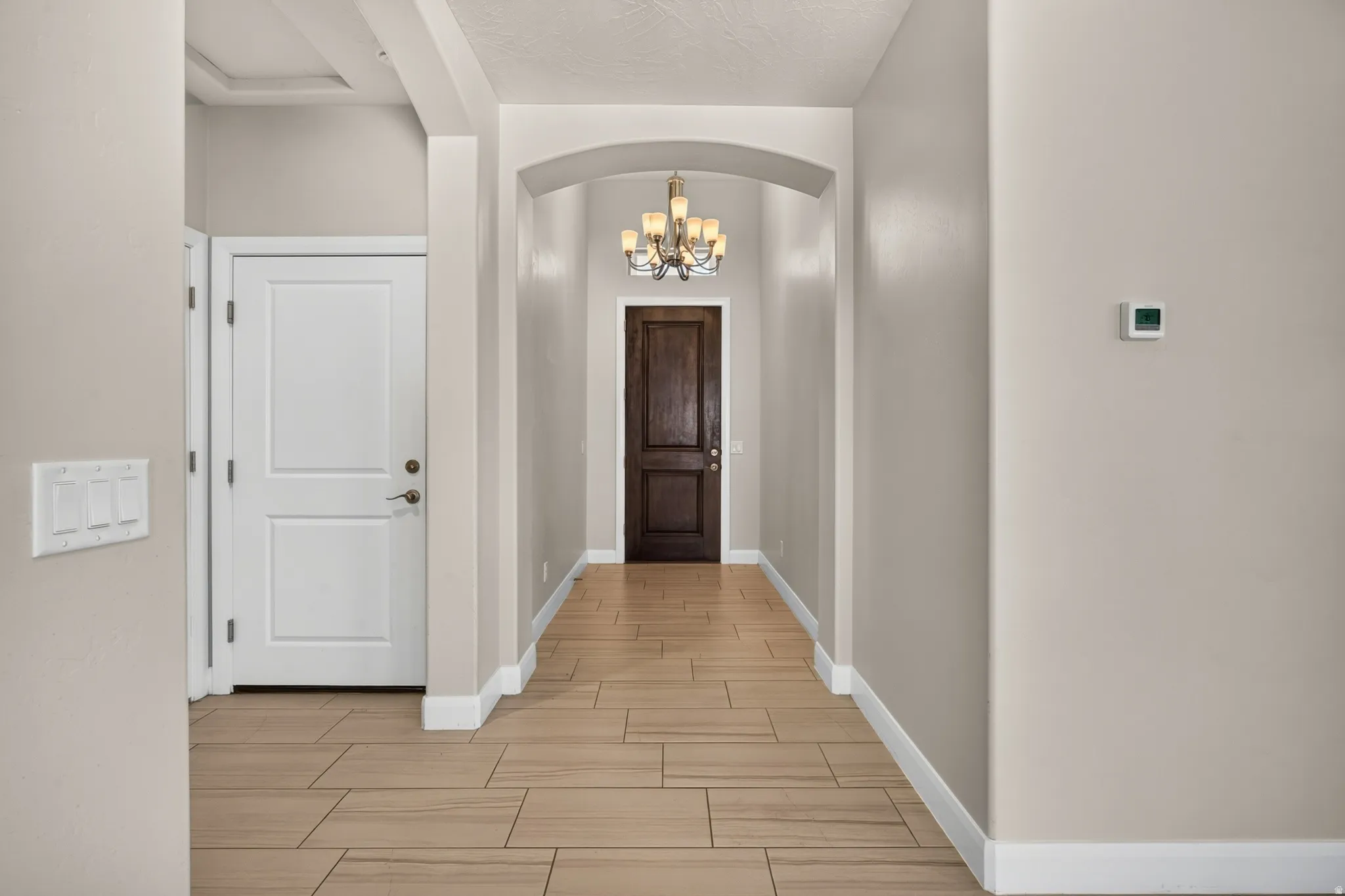 Hallway featuring wood-look tile flooring, an arched entryway, and a decorative chandelier