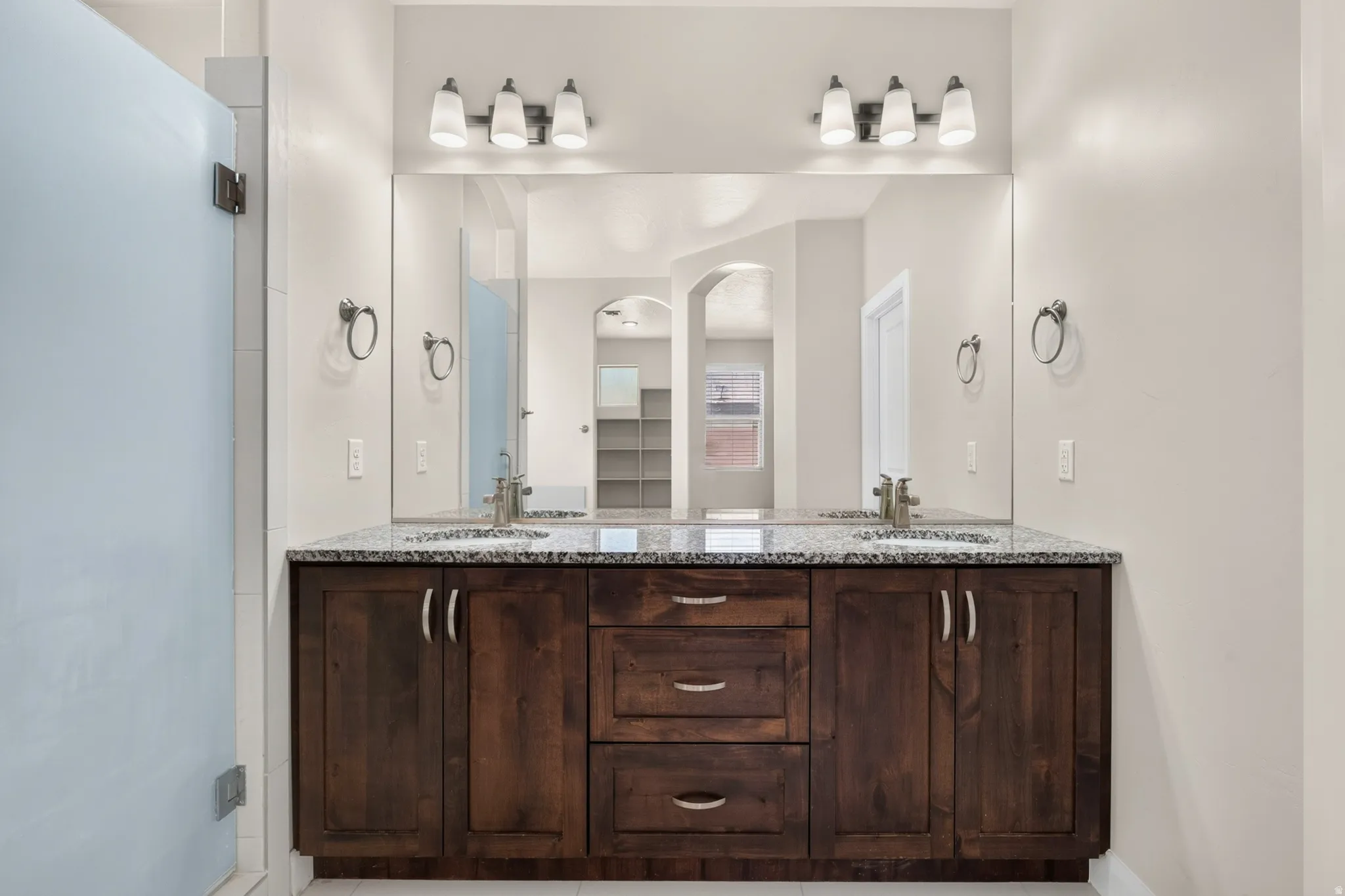 Dual vanity featuring a granite countertop, undermount sinks, and wood-finish cabinetry