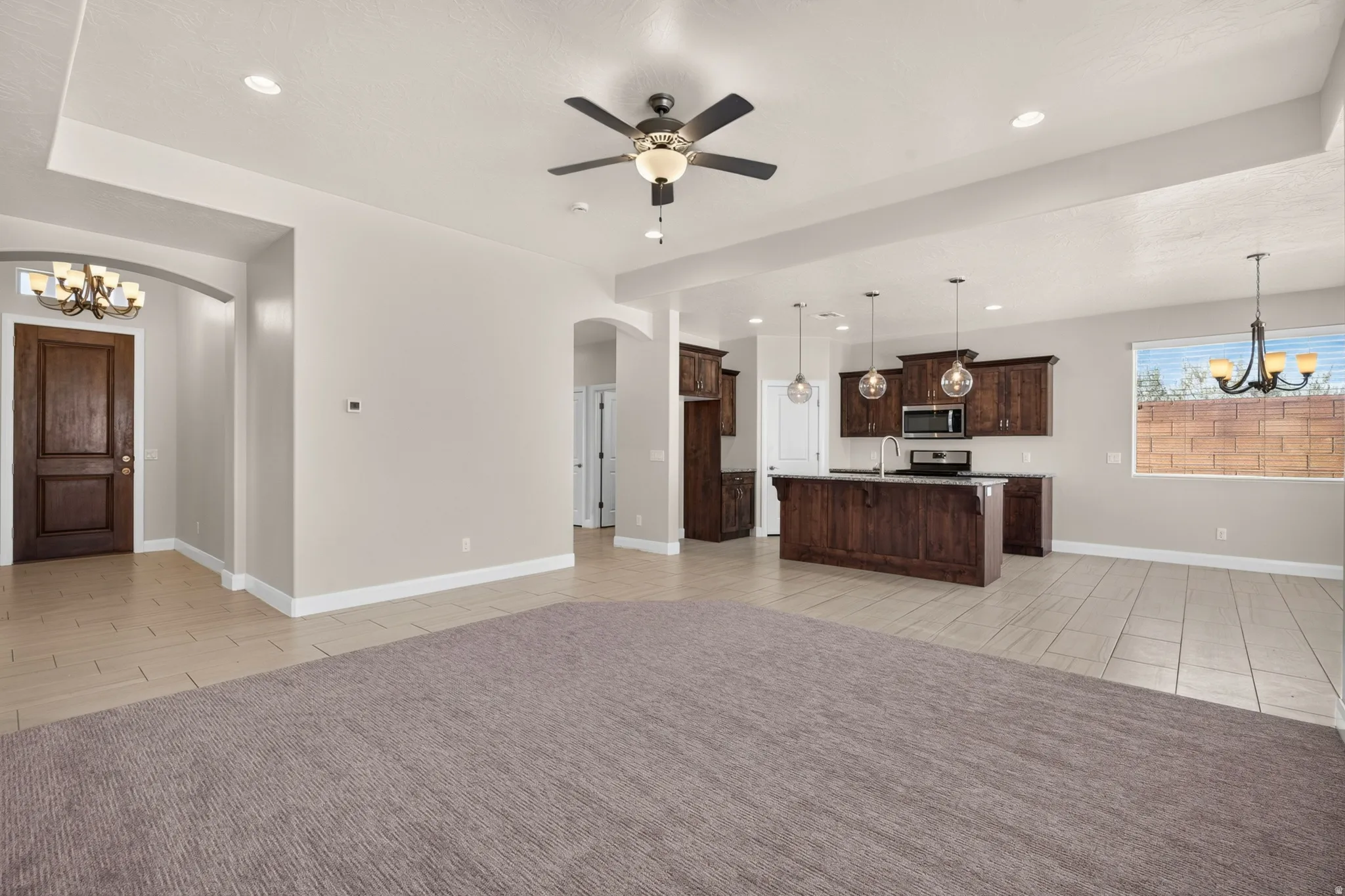 Spacious room featuring tray ceilings, a ceiling fan with integrated lighting, recessed lighting, and mixed flooring with carpet and tile