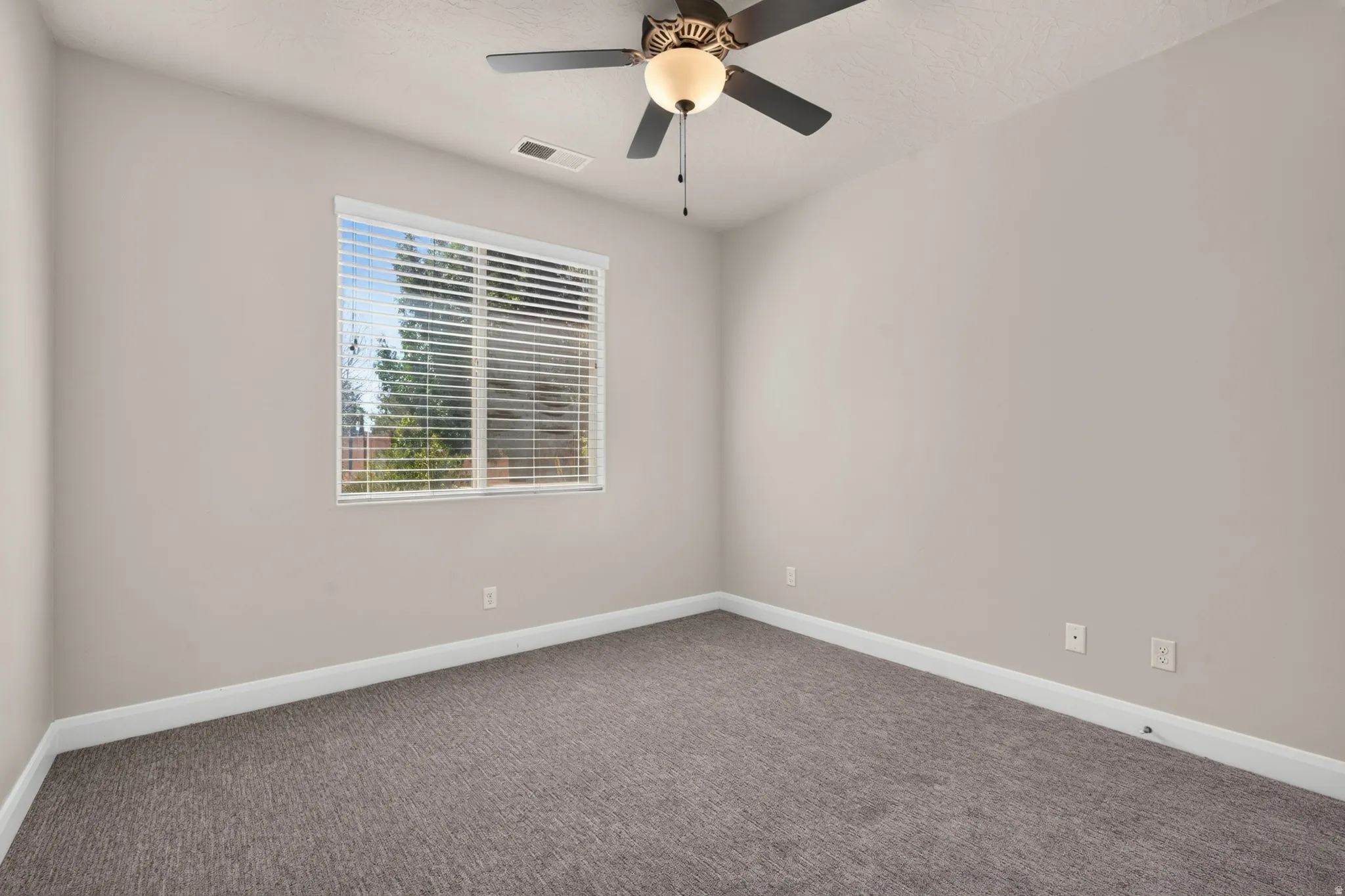 Neutral wall color, textured carpeting, window with horizontal blinds, and a ceiling fan with integrated lighting