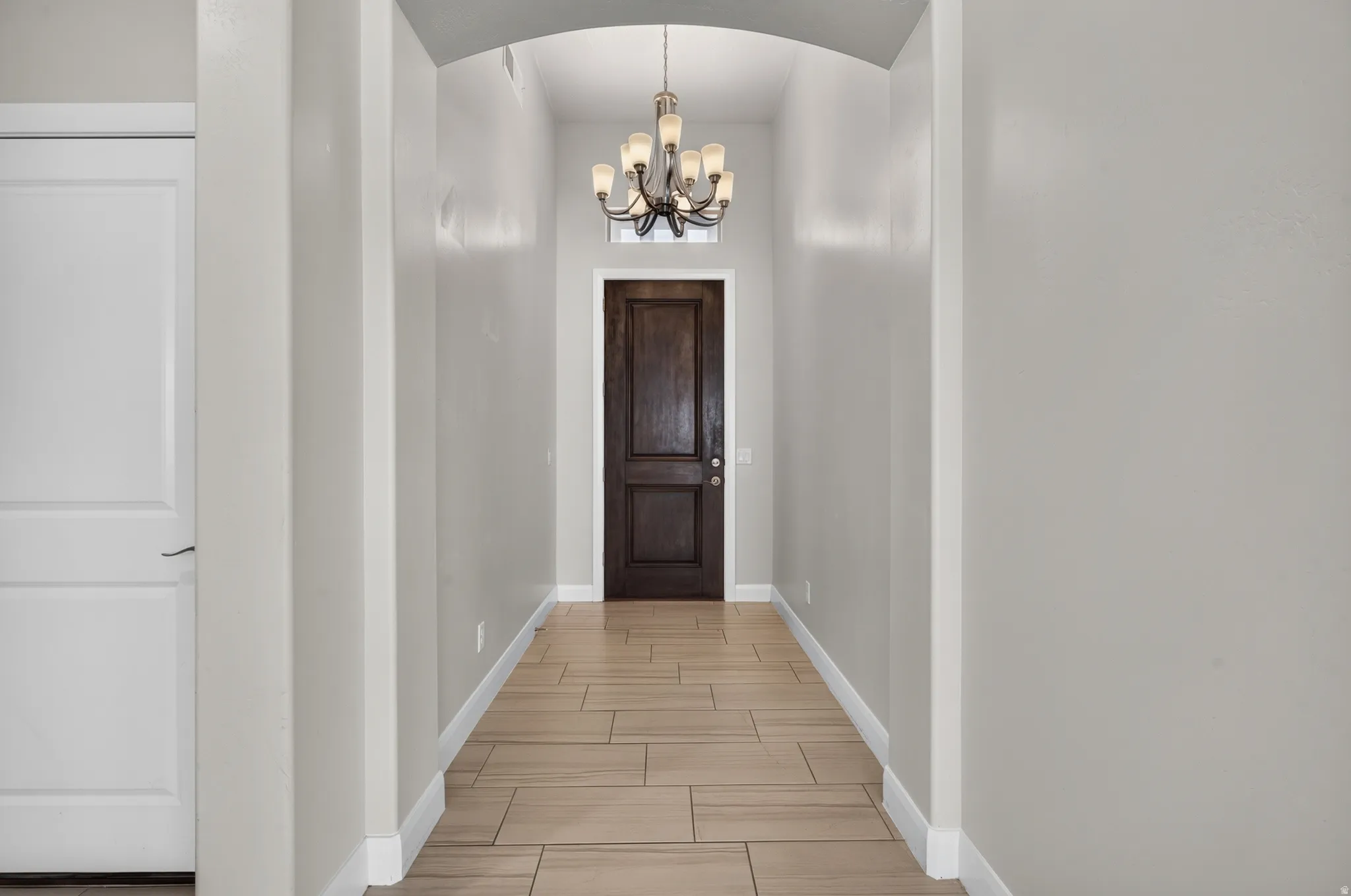Arched entryway featuring wood-finish tile flooring and a decorative chandelier