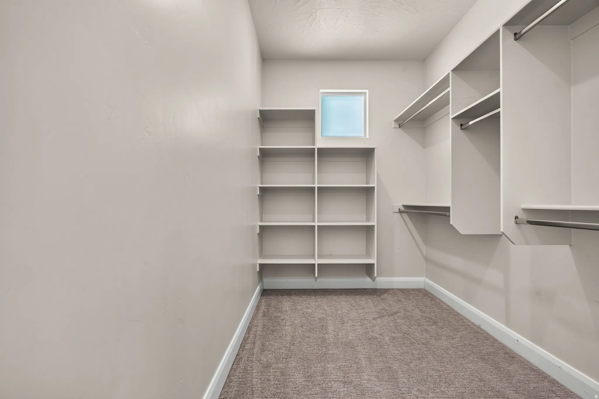 Built-in shelving, hanging rods, square window, and carpeted flooring