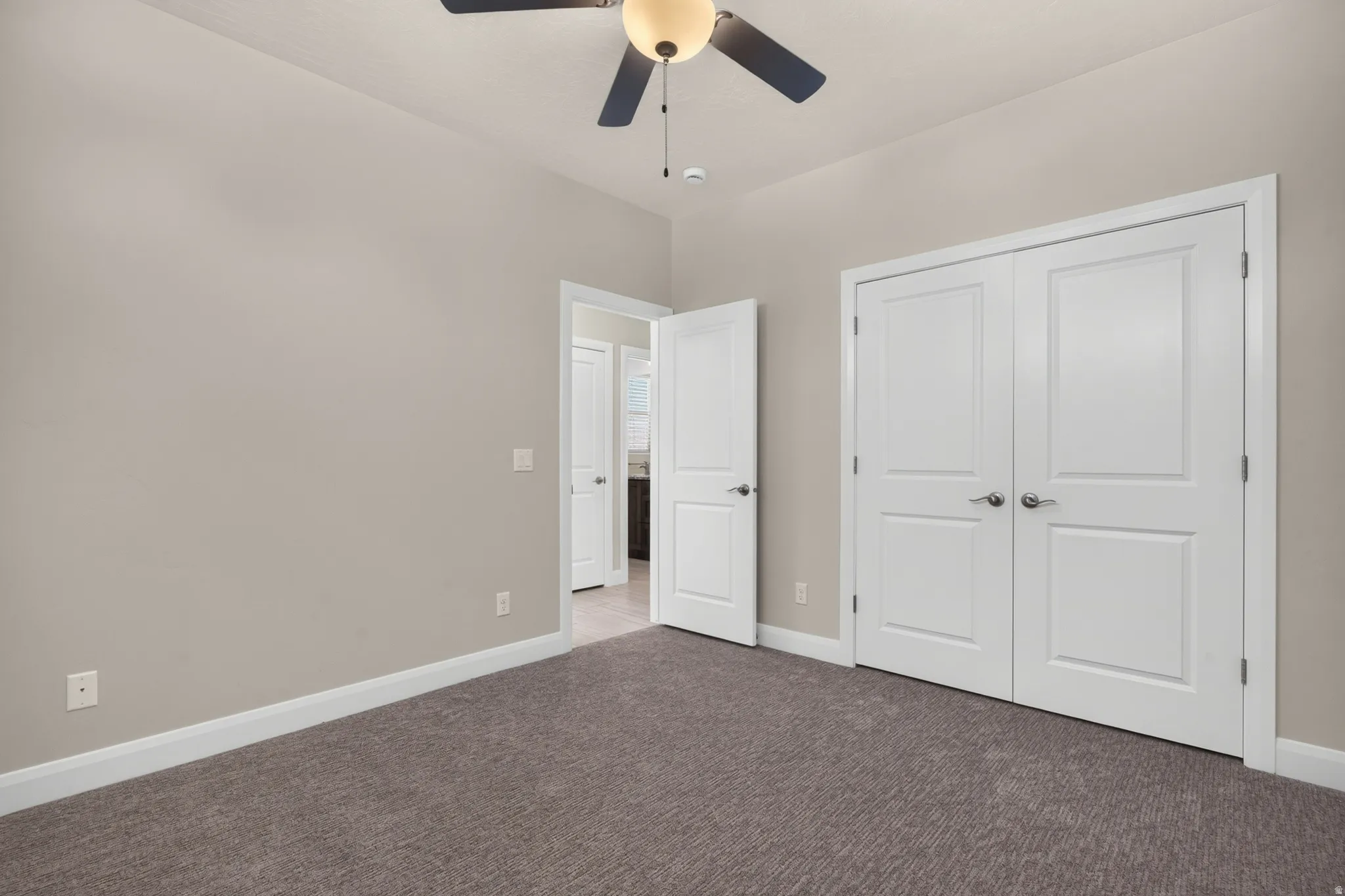 Neutral tone walls, carpeted flooring, a ceiling fan with integrated lighting, and white paneled doors