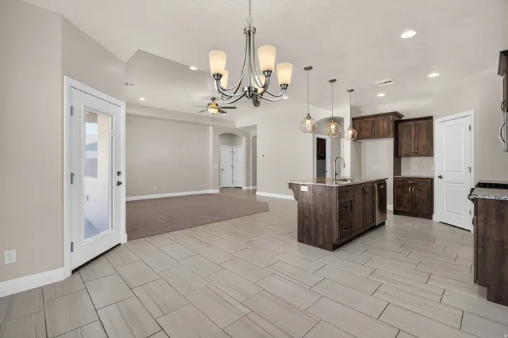 Open-concept living space with vaulted ceilings, large format tile flooring, a kitchen island with pendant lighting, and dark wood-finish cabinetry
