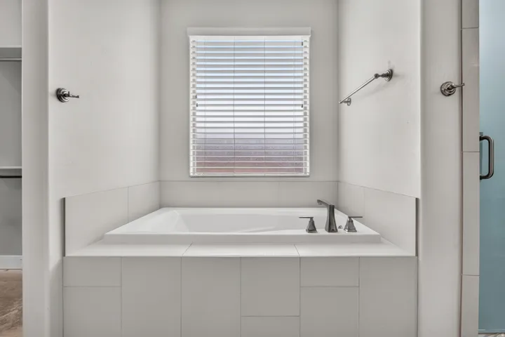 Alcove bathtub with white tile surround, built-in deck-mount faucet, and window with horizontal blinds