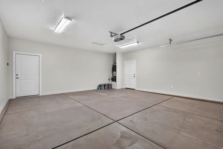 Spacious garage with light gray walls, two bright overhead light fixtures, a garage door opener mechanism, and a concrete floor