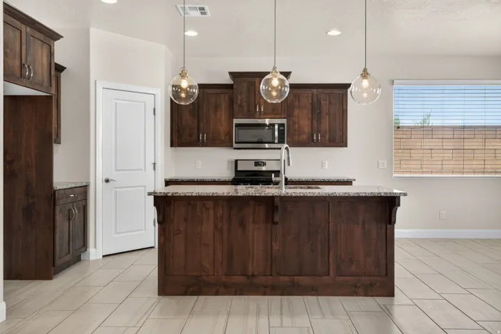 Kitchen featuring dark wood-finish cabinetry, granite countertops, stainless steel appliances, and a central island with pendant lighting