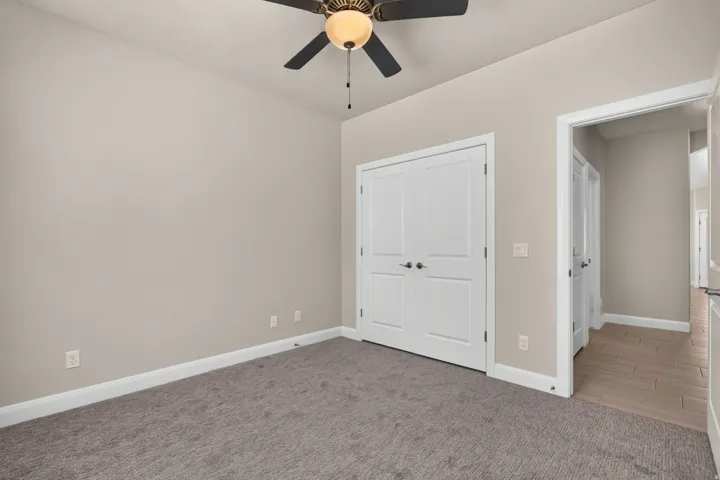Neutral wall tones, gray carpet, permanent ceiling fan, white trim, and a double-door closet