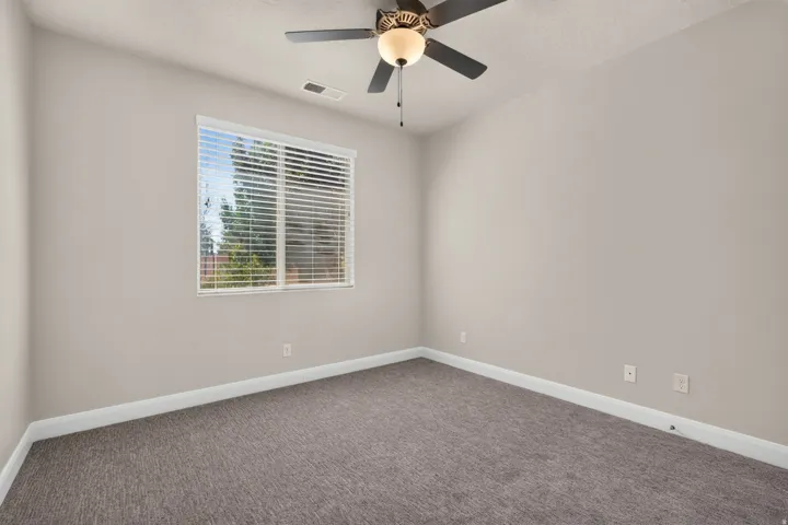 Neutral wall color, textured carpeting, window with horizontal blinds, and a ceiling fan with integrated lighting