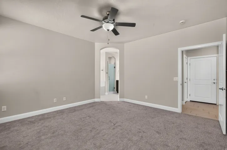 Spacious room with gray carpeting, neutral wall paint, and a ceiling fan