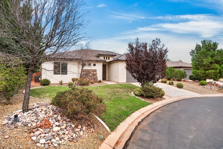 Stucco exterior with stone accents, a landscaped front yard with mature plantings, and a paved driveway