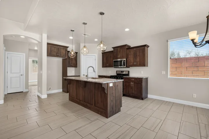 Kitchen featuring dark wood-finish cabinetry, stainless steel appliances, a central island with a sink, and pendant lighting
