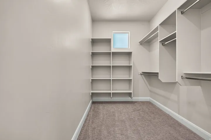 Built-in shelving, hanging rods, square window, and carpeted flooring