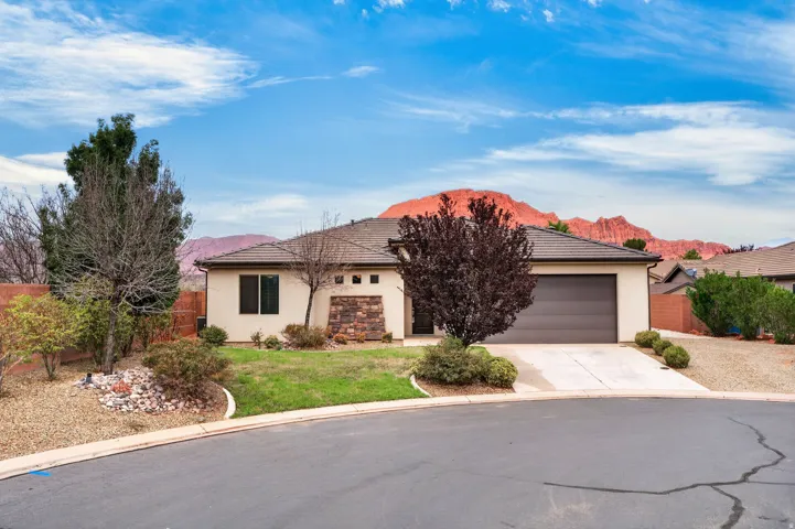 Stucco exterior with stone accents, attached garage, concrete driveway, tiled roof, and xeriscaped and lawn landscaping