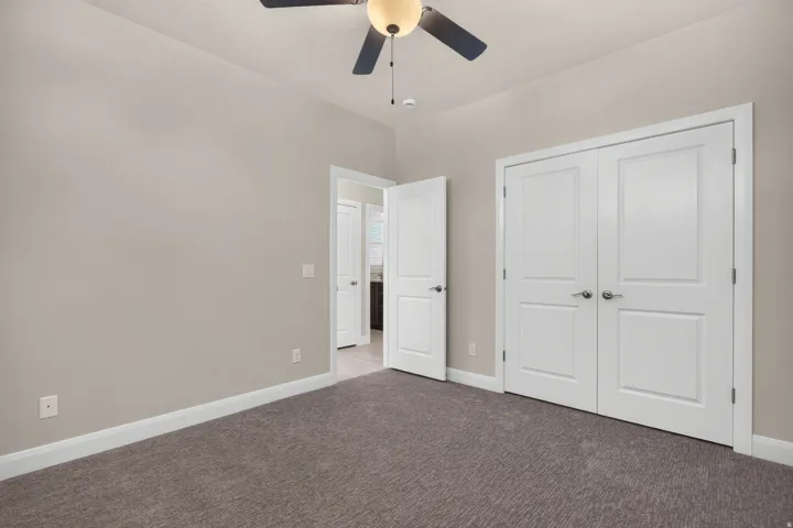 Neutral tone walls, carpeted flooring, a ceiling fan with integrated lighting, and white paneled doors