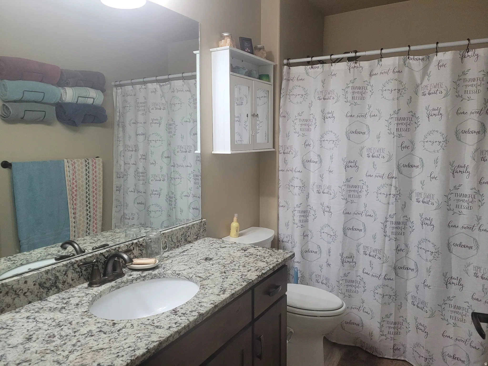 Granite-look countertop with an oval undermount sink, bronze-finish faucet, and coordinating dark wood-finish cabinetry