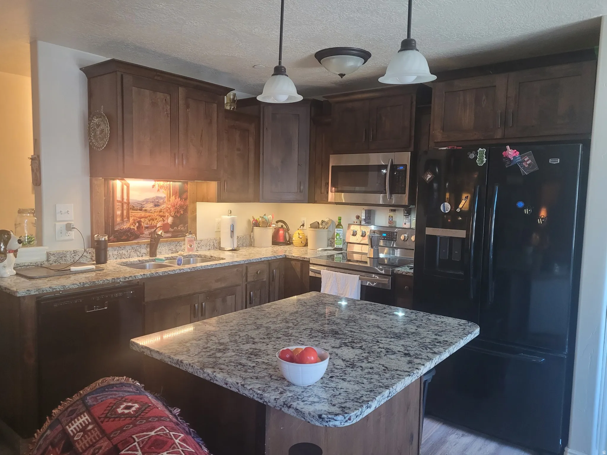 Kitchen featuring dark wood cabinetry, granite countertops, a stainless steel microwave, and a black French door refrigerator
