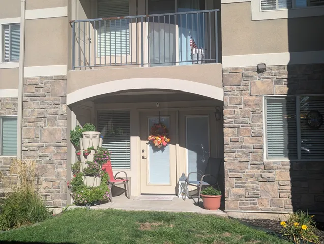Stone facade exterior with an arched entryway, ground-level windows with blinds, and an upper-level balcony with metal railings