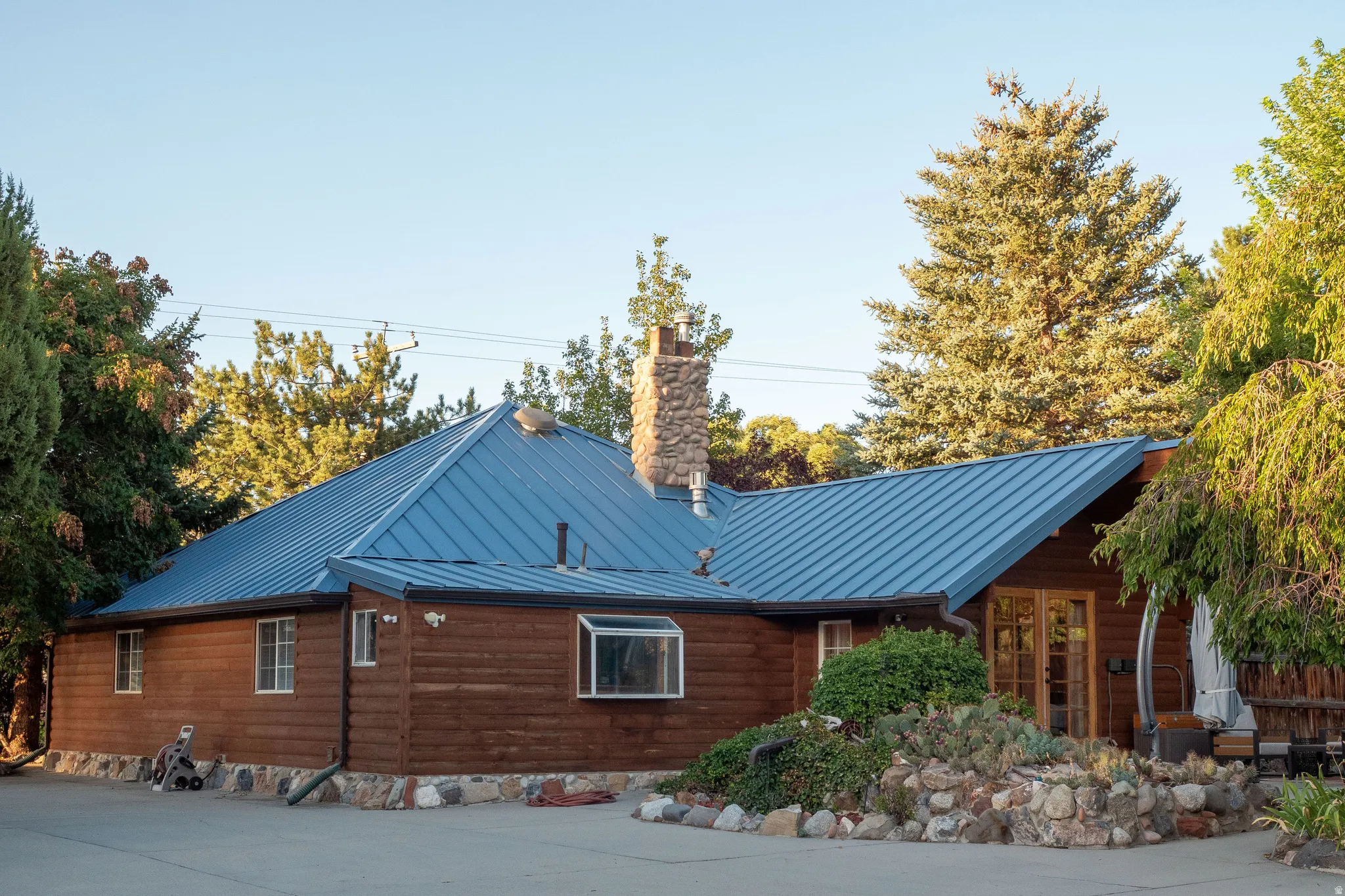 Blue metal roof, wood-paneled exterior, stone chimney, stone foundation, and multiple windows
