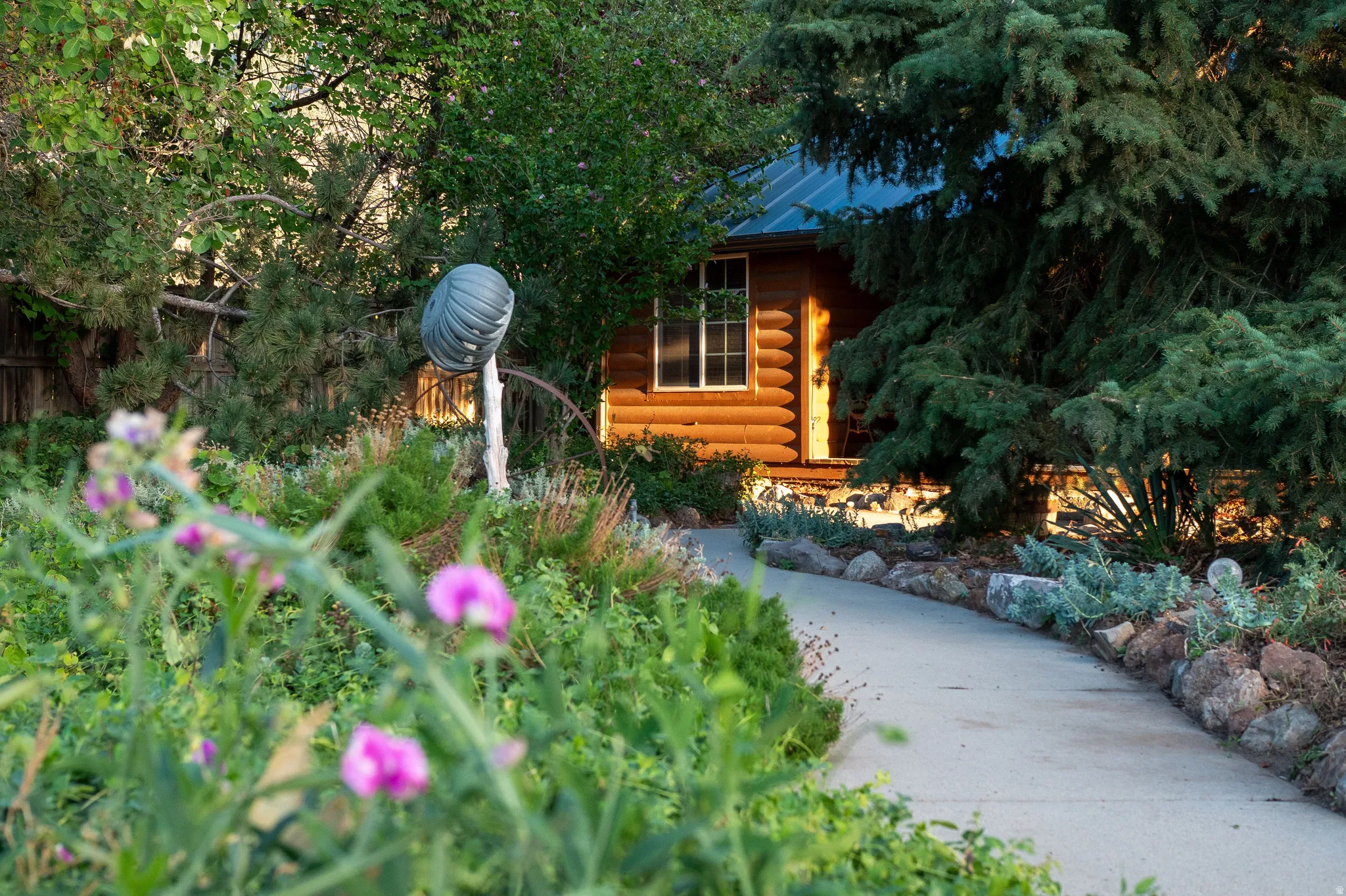 Log cabin exterior, mature trees, concrete pathway, extensive landscaping, and rock garden elements