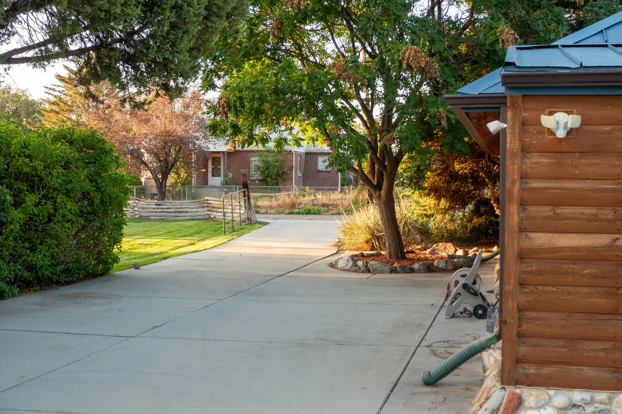 Paved driveway leading to a structure with wood siding, a blue metal roof, and stone base