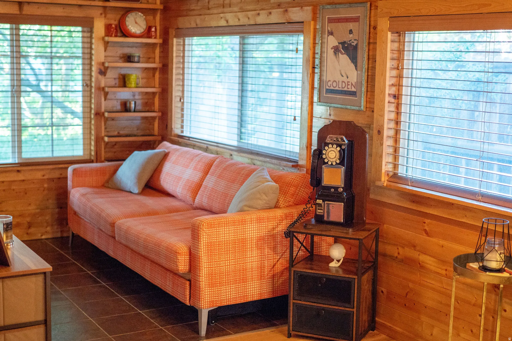 Wood-paneled interior walls, natural wood window frames, large windows with horizontal blinds, built-in wooden shelving, and dark tile flooring