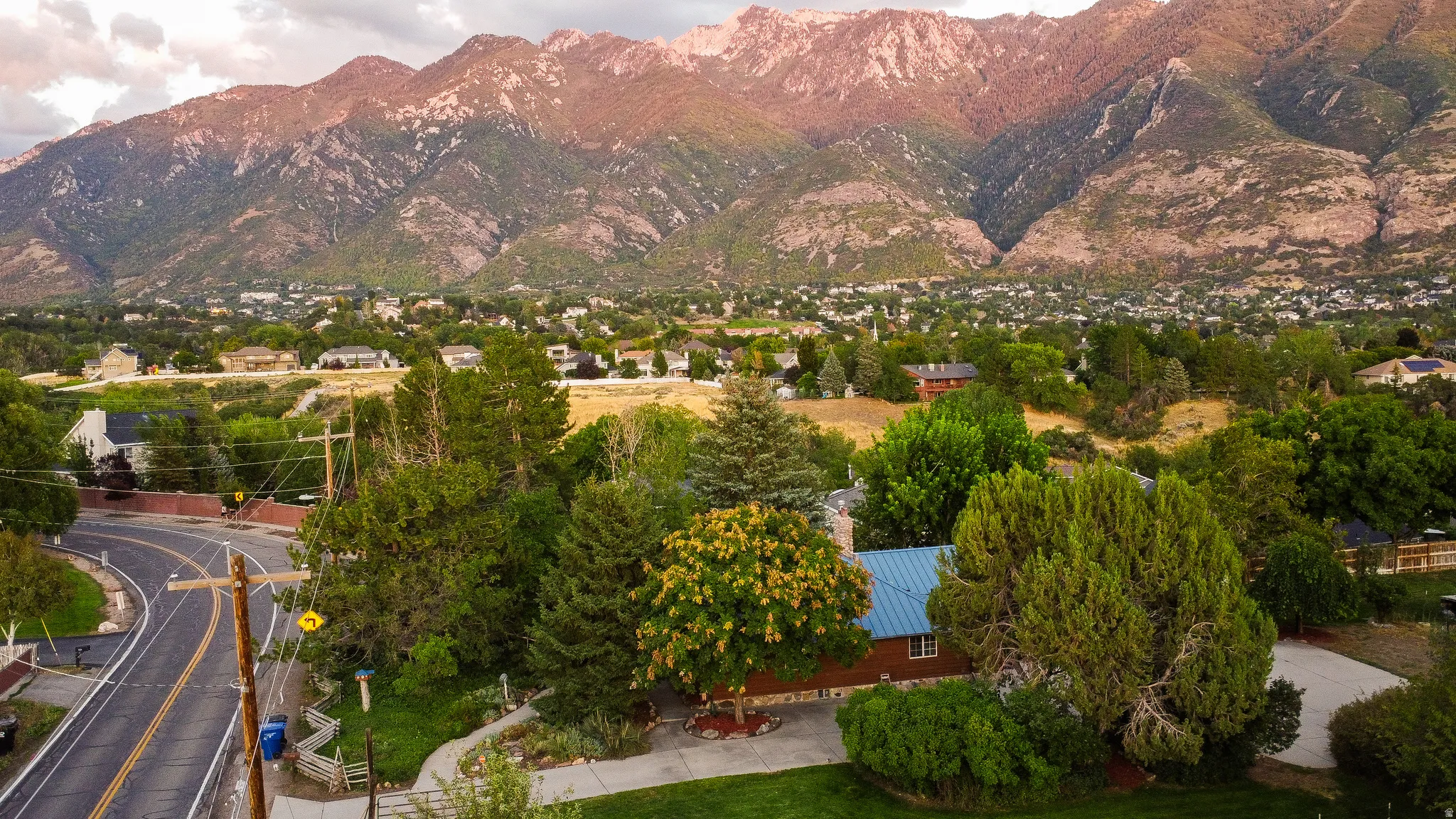 Mountain backdrop, residential area, mature trees, paved road, manicured landscaping