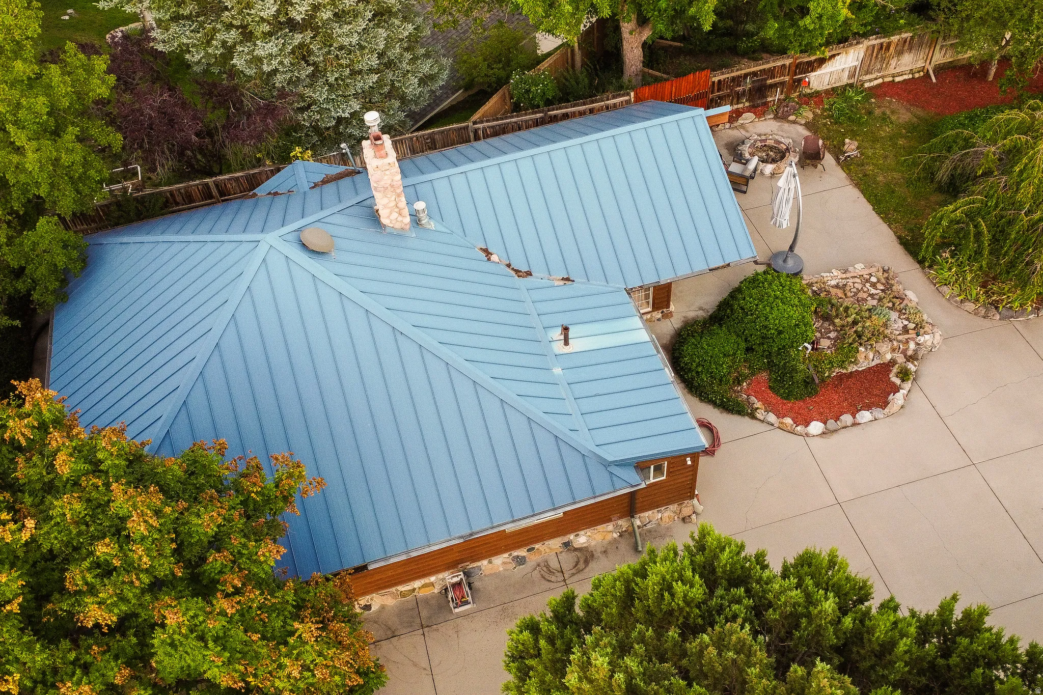 Blue metal roof, stone chimney, wood siding, concrete patio, and landscaped rock garden