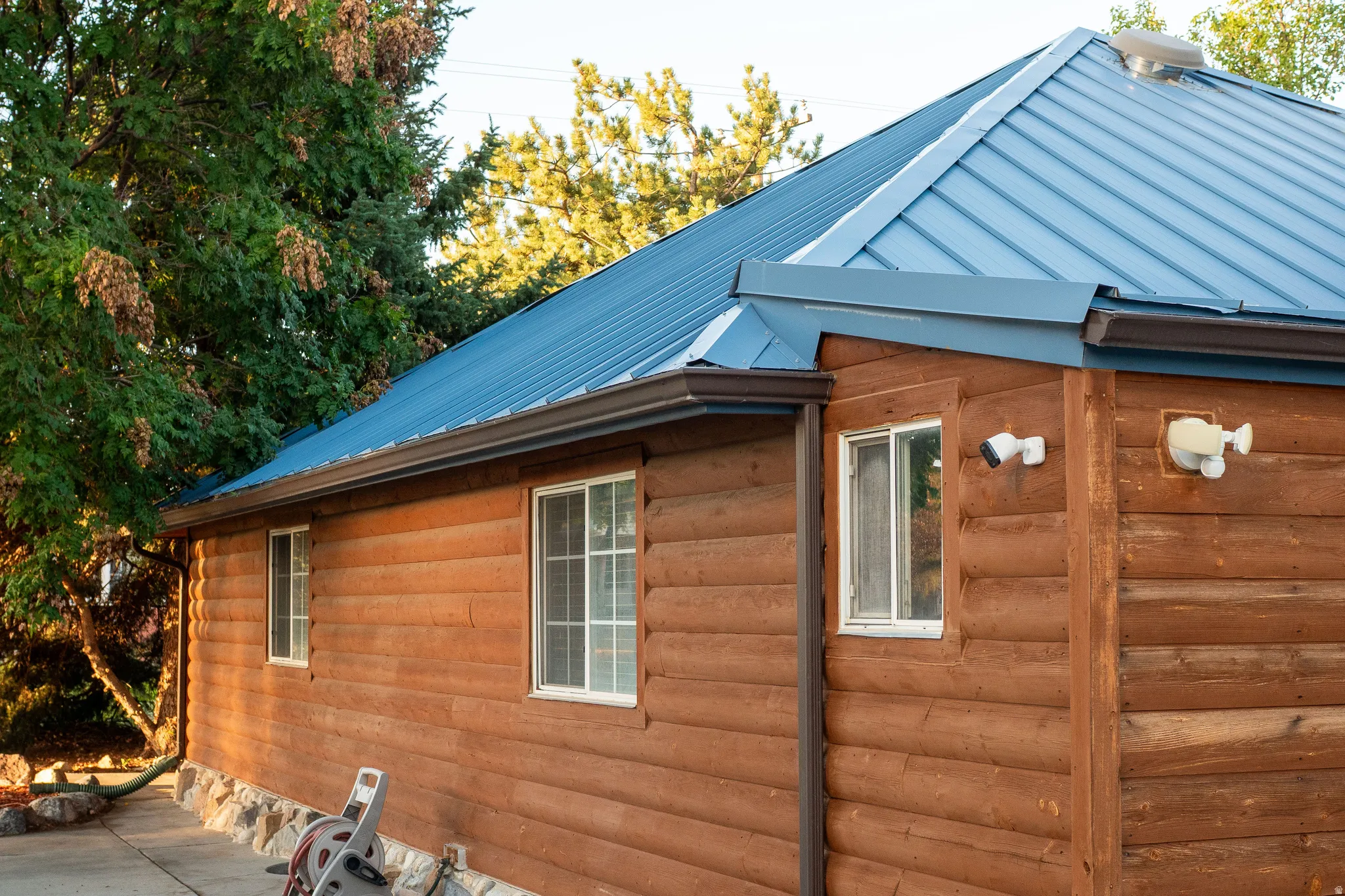 Log siding exterior with a blue metal roof, white-framed windows, and a stone foundation