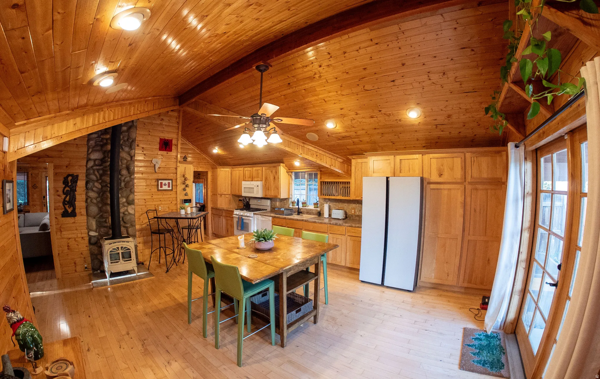Vaulted wood-paneled ceilings, wood-finish flooring, stone-clad fireplace with wood-burning stove, natural wood cabinetry, and French doors