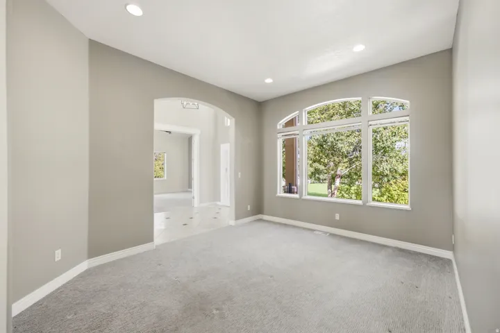 Recessed lighting, arched doorway, large picture windows, light gray wall paint, and gray carpet flooring