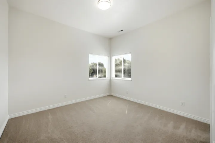 Neutral tone wall paint, carpeted flooring, corner windows with blinds, flush mount ceiling light fixture