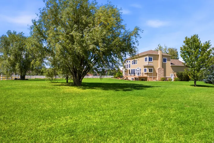 Expansive lawn with mature trees, stucco exterior, multi-level decking, and numerous windows