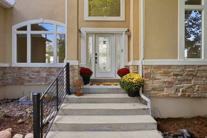 Front entry featuring concrete steps, wrought iron railing, decorative glass door, and stone veneer accents