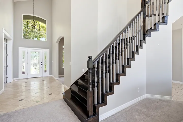 Foyer with high ceilings, an arched transom window, a dark wood staircase with decorative balusters, and patterned tile flooring