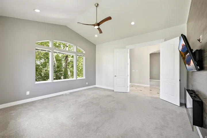 Vaulted ceiling with a ceiling fan and recessed lighting, large arched window, double panel doors, and textured accent wall
