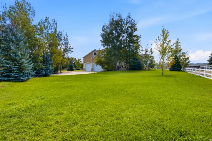 Expansive lawn with mature trees, a two-car garage, and a white picket fence