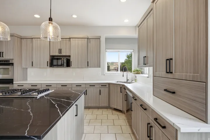 Kitchen featuring light wood-finish cabinetry with black hardware, black island with white veining, white countertops, tile flooring, and stainless steel appliances