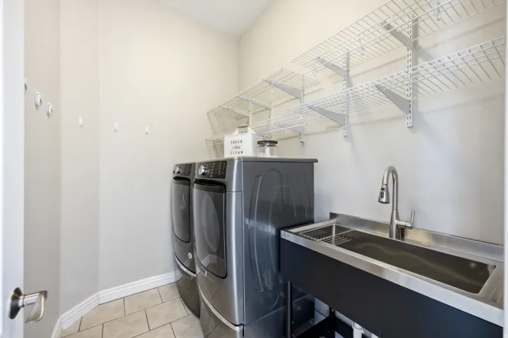 Tile flooring, built-in wire shelving, stainless steel utility sink, and wall-mounted hooks