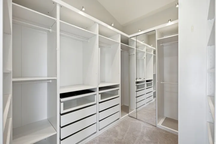 Custom built-in closet system with multiple shelving units, integrated drawers, hanging rods, recessed ceiling lighting, and mirrored closet doors