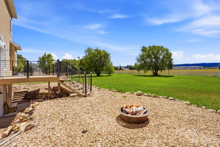 Exterior deck with dark metal railings, gravel patio featuring a fire pit, and expansive green lawn