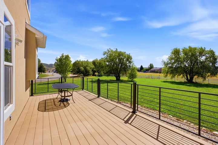 Expansive deck featuring composite decking and a cable railing system, overlooking a large green pasture with mature trees