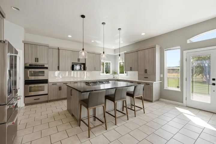 Kitchen featuring stainless steel double ovens, a built-in microwave, a central island with a cooktop, and pendant lighting