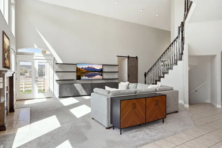Vaulted ceiling, built-in entertainment center with open shelving, double French doors with an arched transom, wood-finish staircase with wrought iron balusters, and a barn door entry