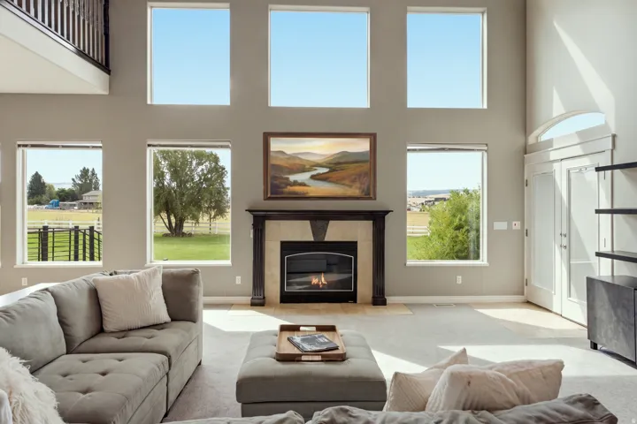 Two-story living area with multiple windows, a fireplace with a stone surround and wood mantel, and an arched transom above double doors